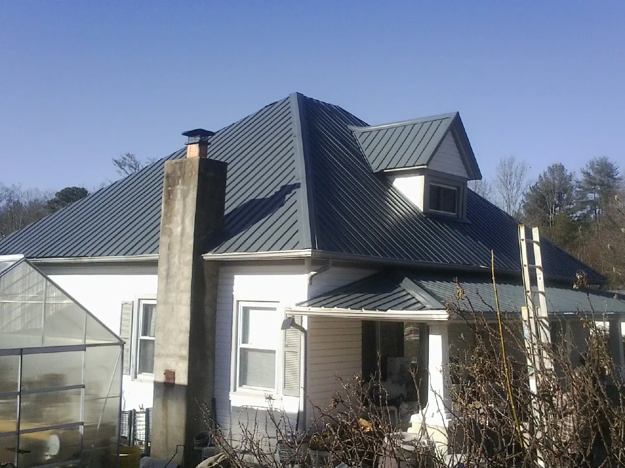 Dark blue standing seam metal roof on a white farmhouse with dormer — Slate & Tile Roof Repair by Roofing Brothers in Rocky Ford