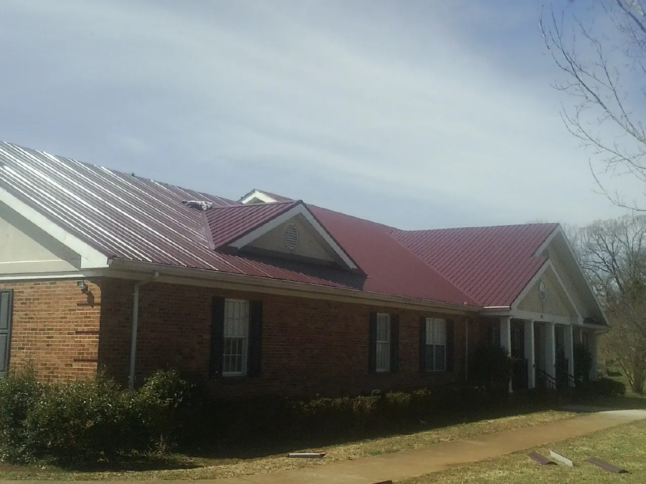 Red metal roof with gabled entries on a long brick building, from a Hail Damage Roof Repair job in Rocky Ford