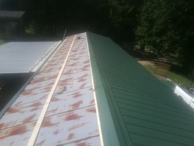 Old rusted panels beside newly installed green metal roofing — Wind Damage Roof Repair by Roofing Brothers in Rocky Ford