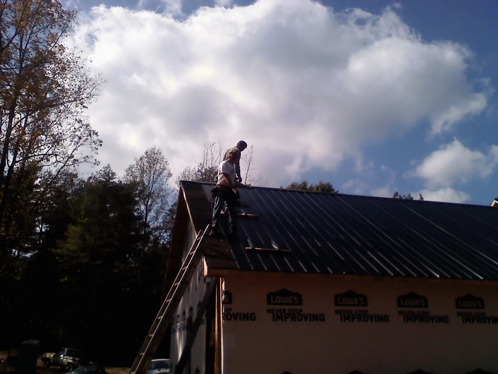 Roofer fastening dark metal panels high against a cloudy sky, from a Roof Inspection job in Rocky Ford
