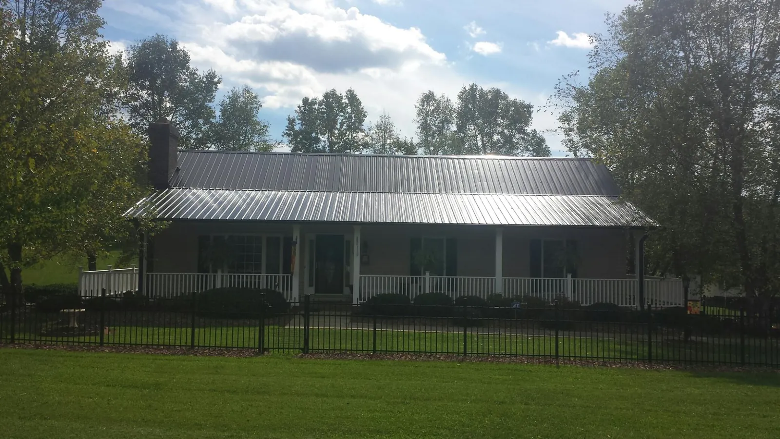 Gray metal roof on a brick ranch with a full width front porch — Gutter Guard Installation work by our crew in Rocky Ford