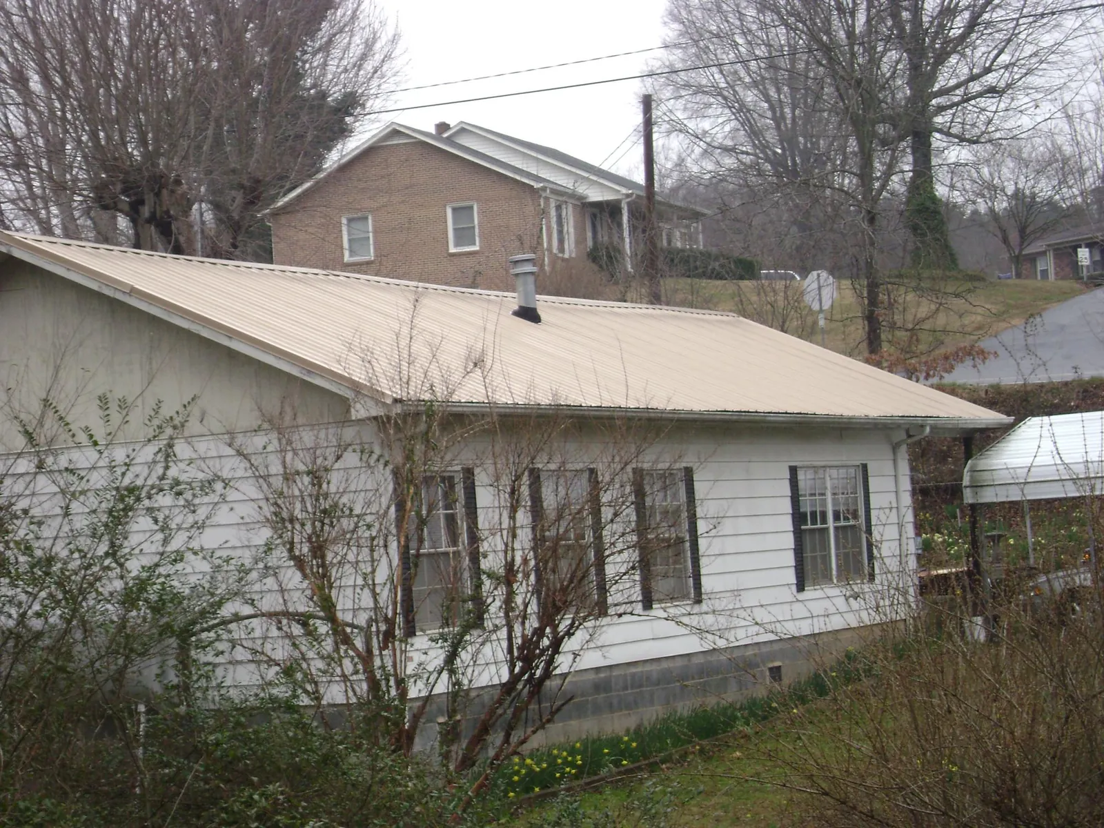 Tan metal roof on a white sided house set into a hillside — Commercial Roofing by Roofing Brothers in Rocky Ford