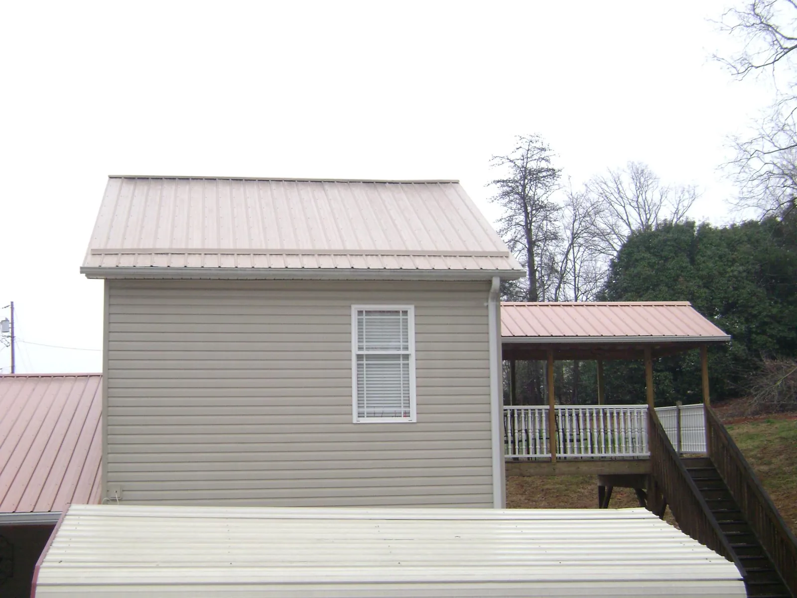 Tan metal roofs on a two story addition and attached porch, from a Roof Replacement job in Rocky Ford